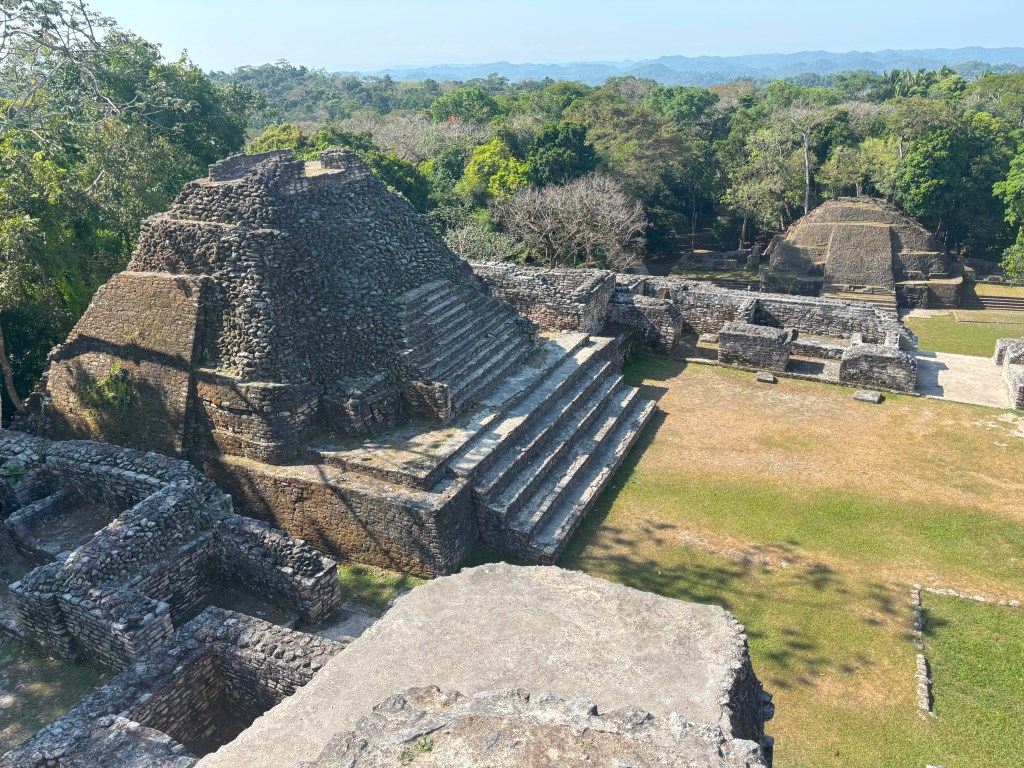 View from the top of a pyramid at Caracol, Belize, showcasing ancient stone structures and lush greenery in the background.